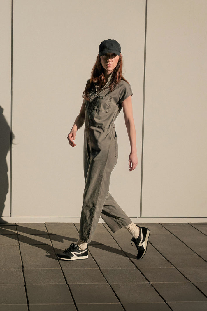 Person wearing a green jumpsuit and black cap walking on a tiled floor.