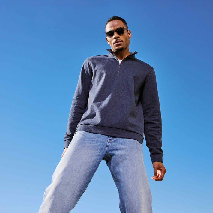 Man wearing a dark blue pullover and light blue DUER jeans against a clear blue sky