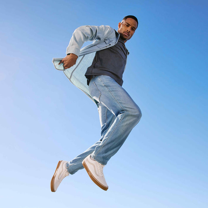 Man in light blue denim outfit jumping against a clear blue sky wearing DUER denim