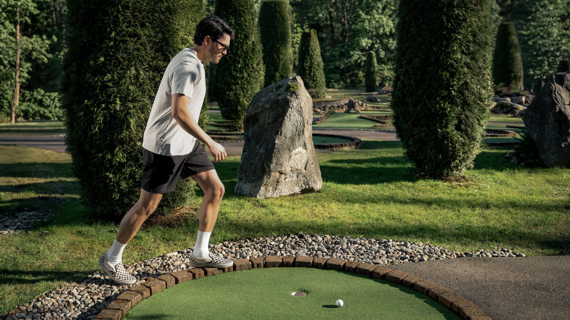 Man playing mini golf on a course in Duer Golf Shorts with trees and rocks in the background
