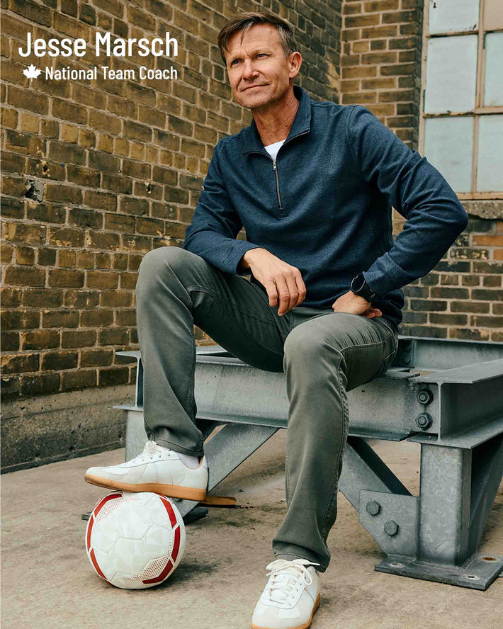 Man sitting on a metal bench with a soccer ball, identified as Jesse Marsch, National Team Coach wearing DUER no sweat gull