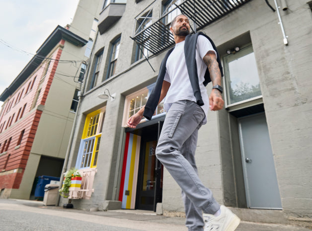 A man dressed in a white T-shirt, gray pants, and white sneakers is walking along a street